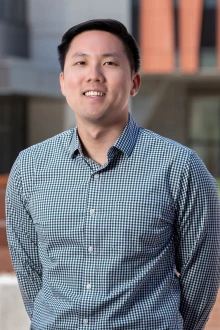 Portrait of a young Asian man wearing a button-up shirt standing outside. 