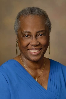 Portrait of a Black woman with greying hair, dangling earrings, wearing a blue blouse