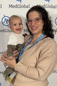 Sommer Aldulaimi, MD, holding a smiling baby in front of a MedGlobal backdrop.