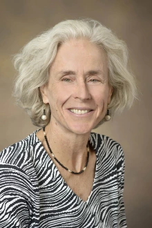 Portrait of Maia Ingram wearing a black and white striped shirt in front of a beige background.