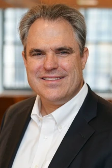 A portrait of Justin Starren, MD, PhD, in a white shirt and black jacket.