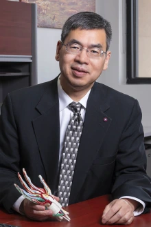 Alt Text: Portrait of Zong-Ming Li sitting at his office desk holding an anatomical model of the inside of a hand.