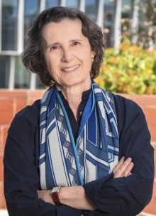 Smiling woman in dark blouse and scarf standing outside with arms crossed. 