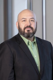 Portrait of a middle aged bald man with a beard wearing a collared shirt and jacket.