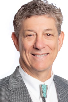 Portrait of middle-aged white man in a suit coat with bola tie. He is smiling. 