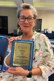 Smiling older woman holds a plaque. 