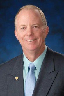 Portrait of a middle-aged balding white man wearing a suit coat and smiling. 